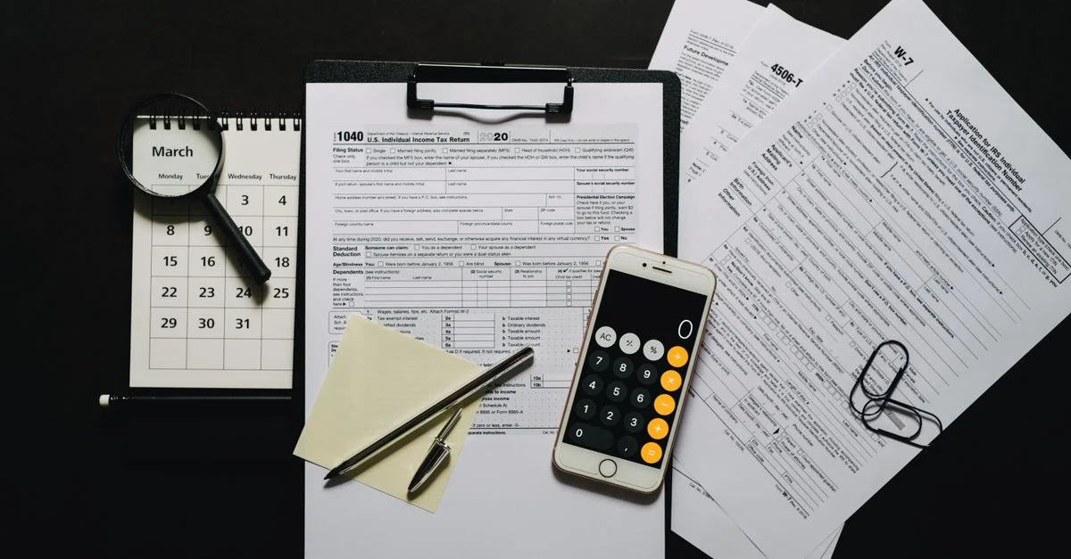Vista superior de documentos fiscales, calculadora, lupa y calendario sobre una superficie negra.