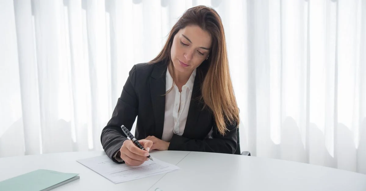 Una mujer profesional en traje firmando papeles en un escritorio, mostrando elegancia corporativa.