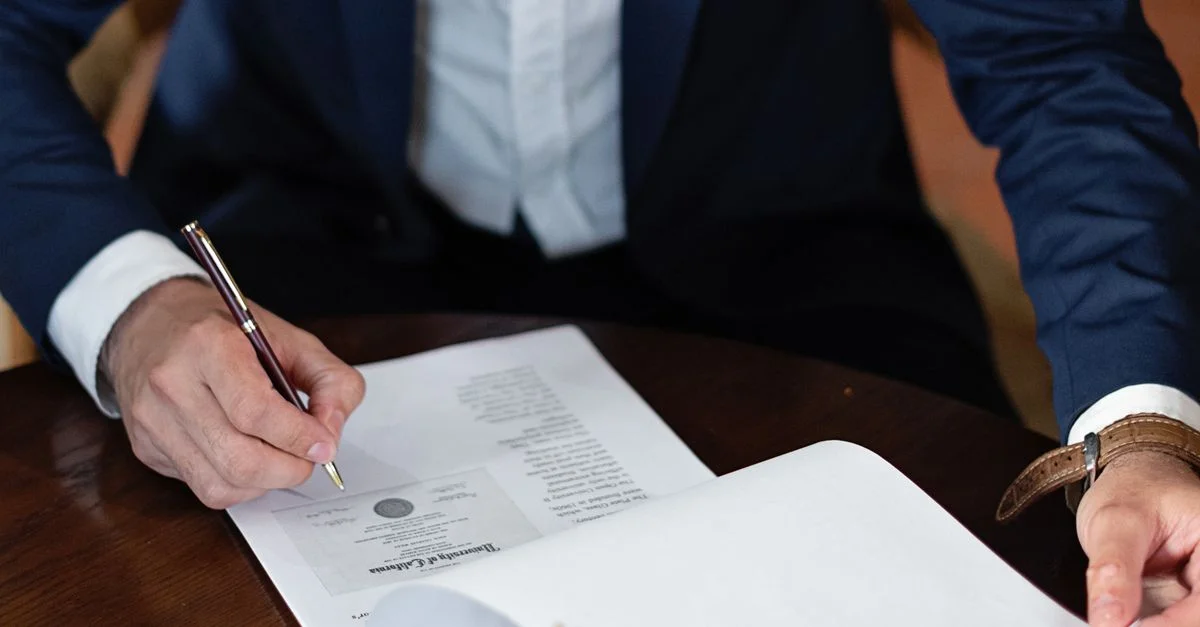 Un profesional firma documentos legales en un escritorio en un entorno de oficina.