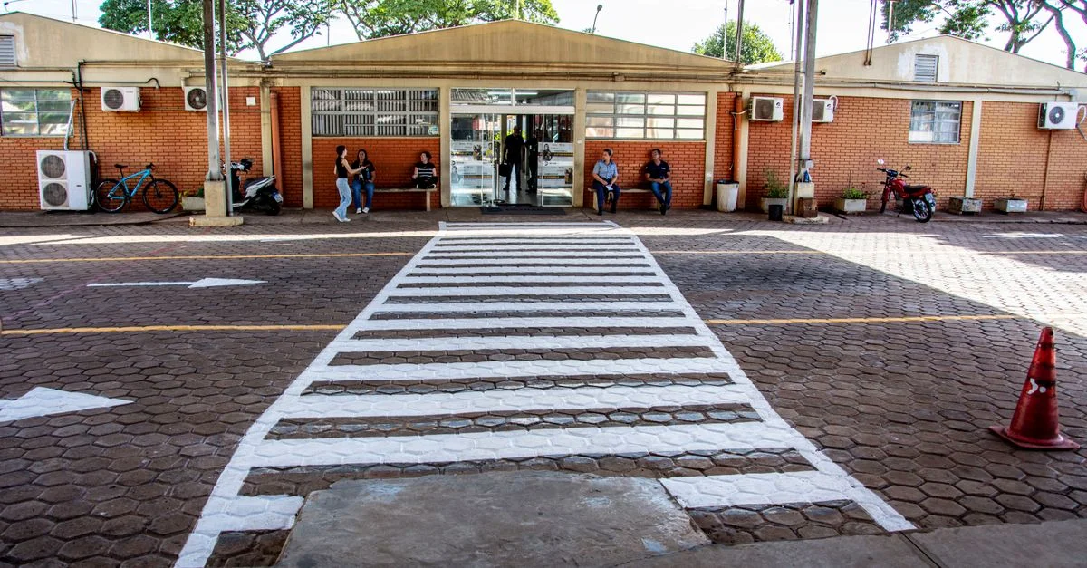 Passage piéton animé à l'entrée d'une installation à Londrina, au Brésil, avec des personnes assises et marchant.