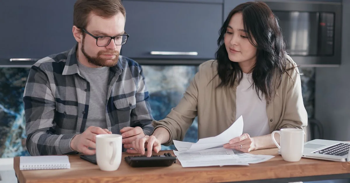 Pareja sentada en casa gestionando las finanzas con documentos y calculadora.