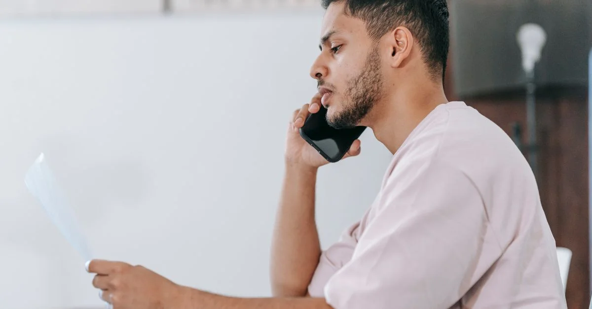 Joven concentrado en una llamada telefónica mientras revisa documentos en su área de trabajo.