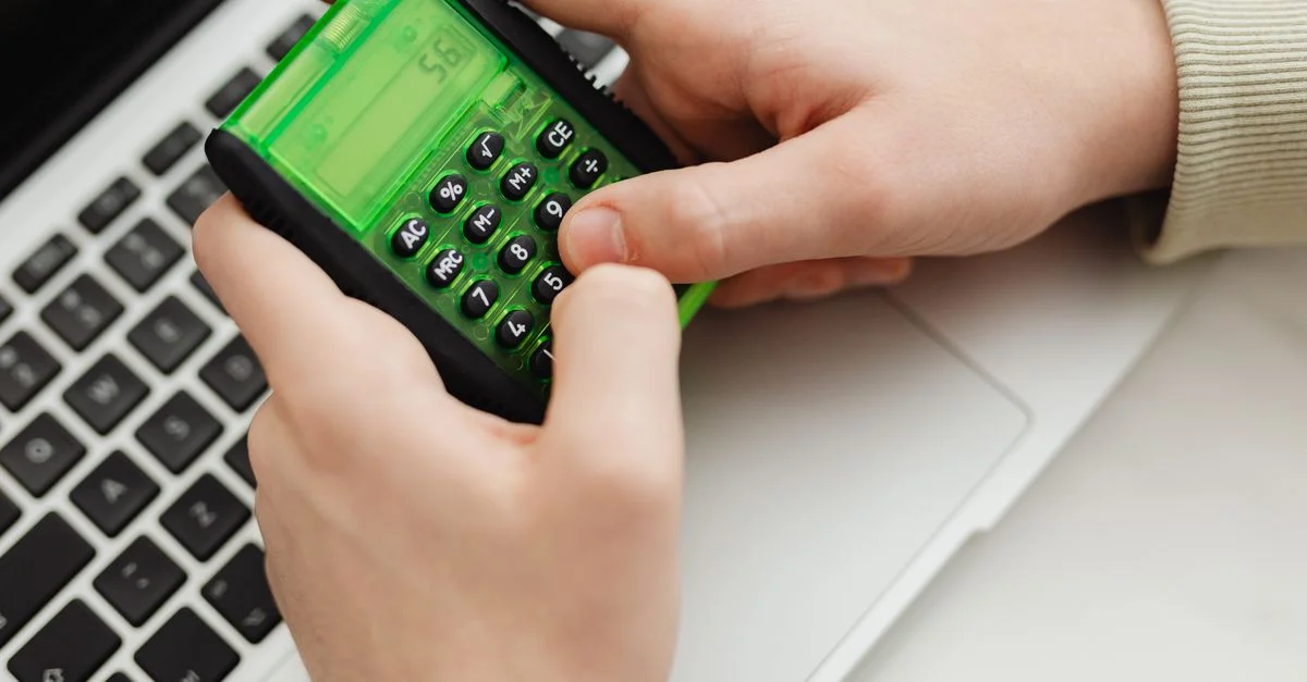 Acercamiento de manos usando una calculadora verde sobre un teclado de laptop, entorno interior.