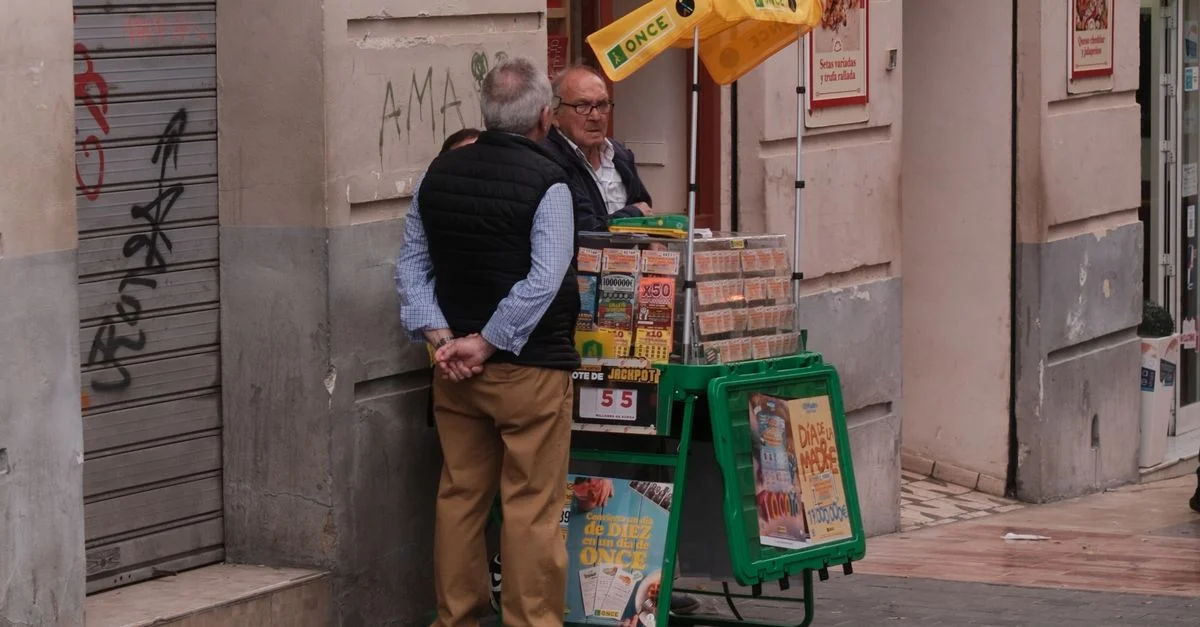 Un vendedor de lotería interactúa con un cliente en una calle de Málaga, España, mostrando una escena de la vida urbana.