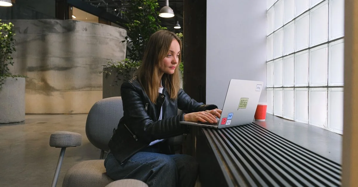 Mujer joven trabajando en una computadora portátil en una oficina moderna y elegante con iluminación natural.