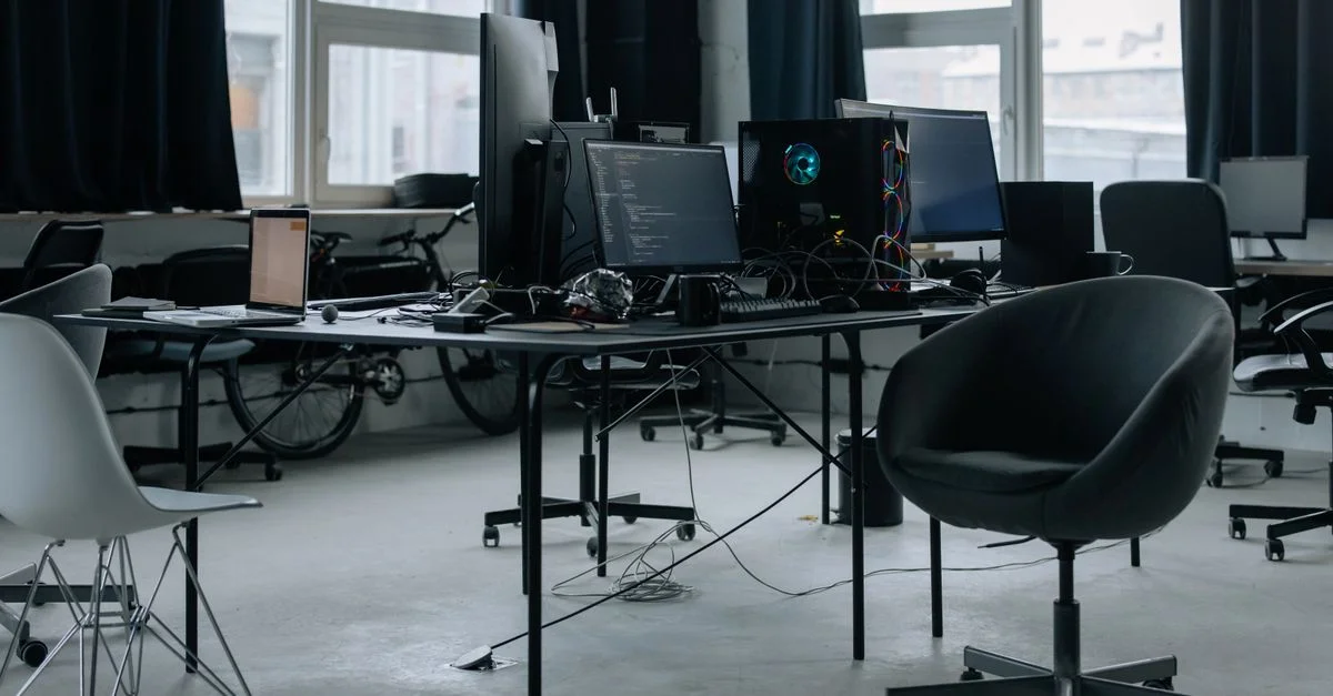 Descubre un espacio de trabajo de oficina moderno con computadoras, sillas y luz natural de grandes ventanas.