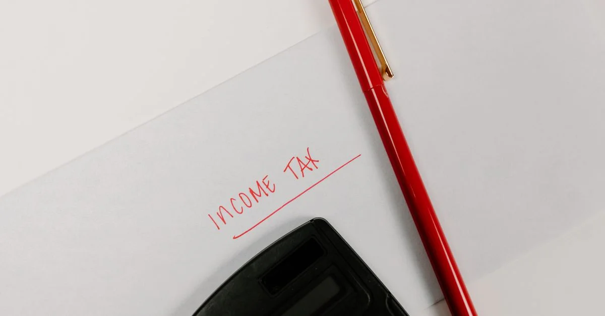 Primer plano de una calculadora y un bolígrafo rojo sobre papel etiquetado 'Impuesto sobre la Renta', representando la planificación financiera.