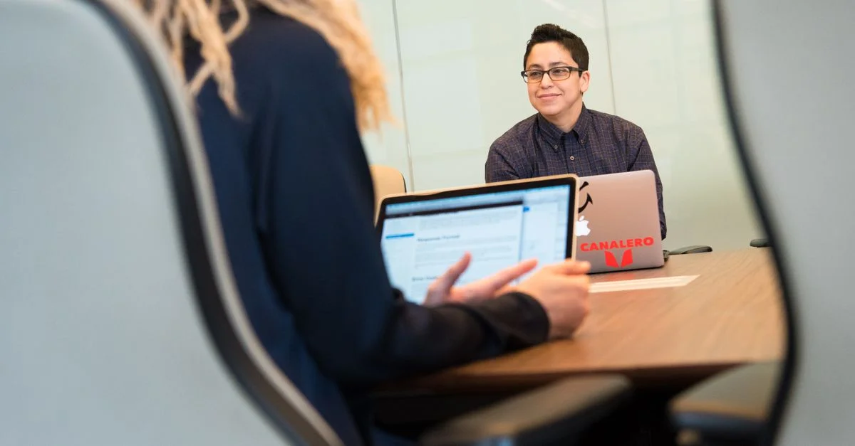 Dos colegas participando en una reunión de negocios con laptops en un entorno de oficina moderno.