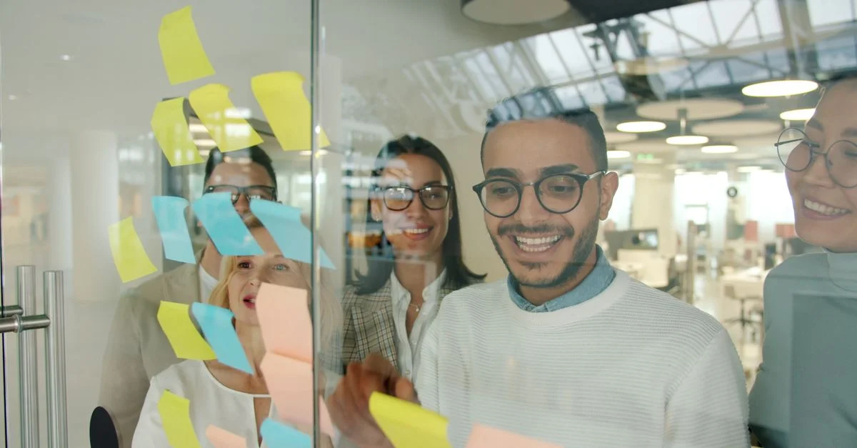 Un equipo sonriente realiza una lluvia de ideas con notas adhesivas en un entorno de oficina moderno.