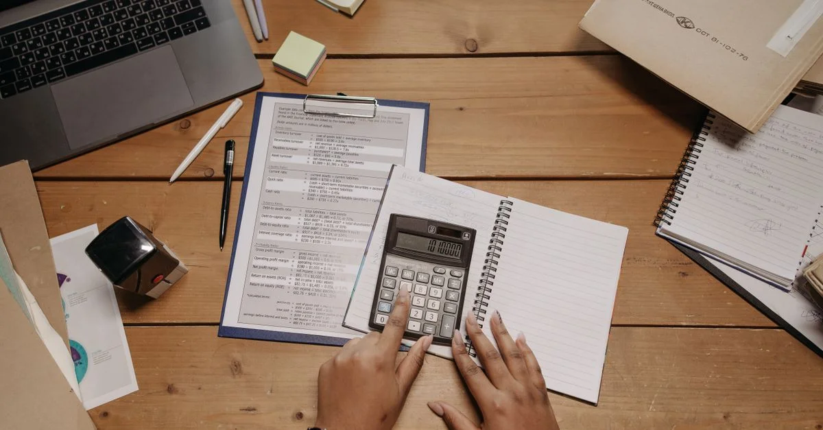 Manos trabajando con calculadora y documentos en un escritorio de madera en un entorno de oficina.