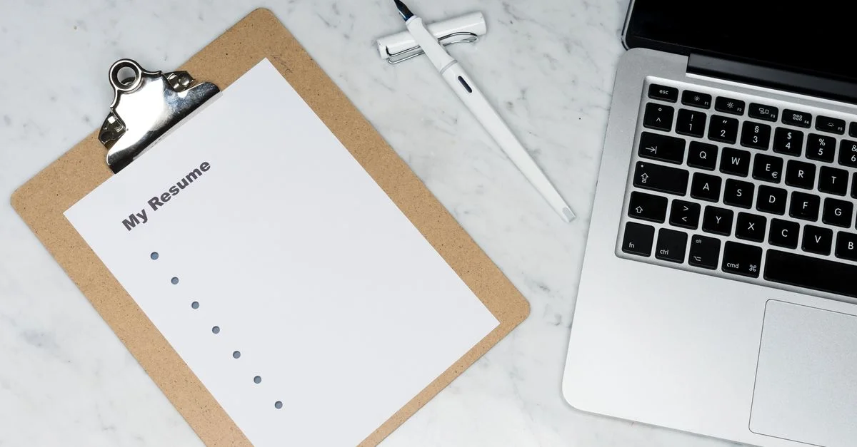 Un portapapeles con un currículum al lado de un bolígrafo y un portátil sobre un escritorio de mármol, ideal para temas de negocios y solicitudes de empleo.