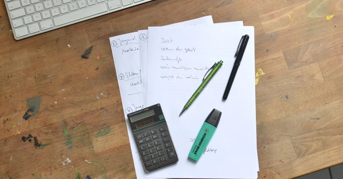 Vista aérea de un escritorio de oficina con documentos, calculadora, teclado y material de papelería para la organización del trabajo.
