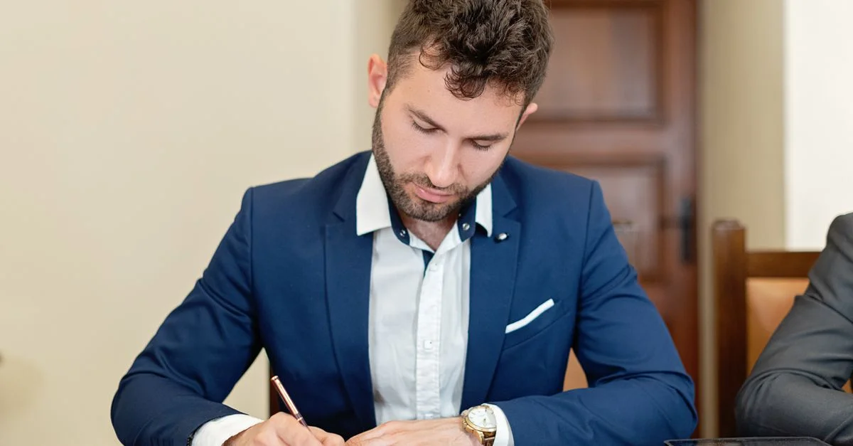 Hombre de negocios seguro en un traje firmando un contrato en el escritorio de la oficina.