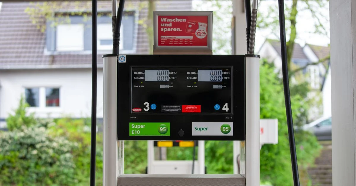 Acercamiento de un surtidor de gasolina en una estación en Bergisch Gladbach, Alemania, con casas visibles alrededor.
