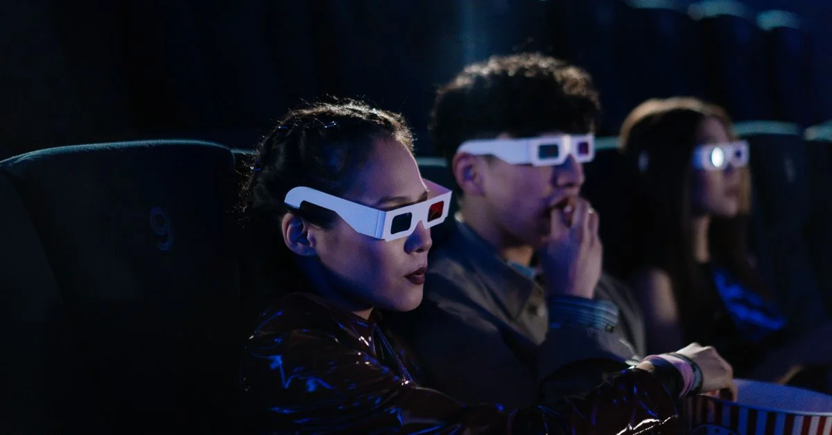 Amigos disfrutando de una noche de película en 3D en el cine, usando gafas y comiendo palomitas.