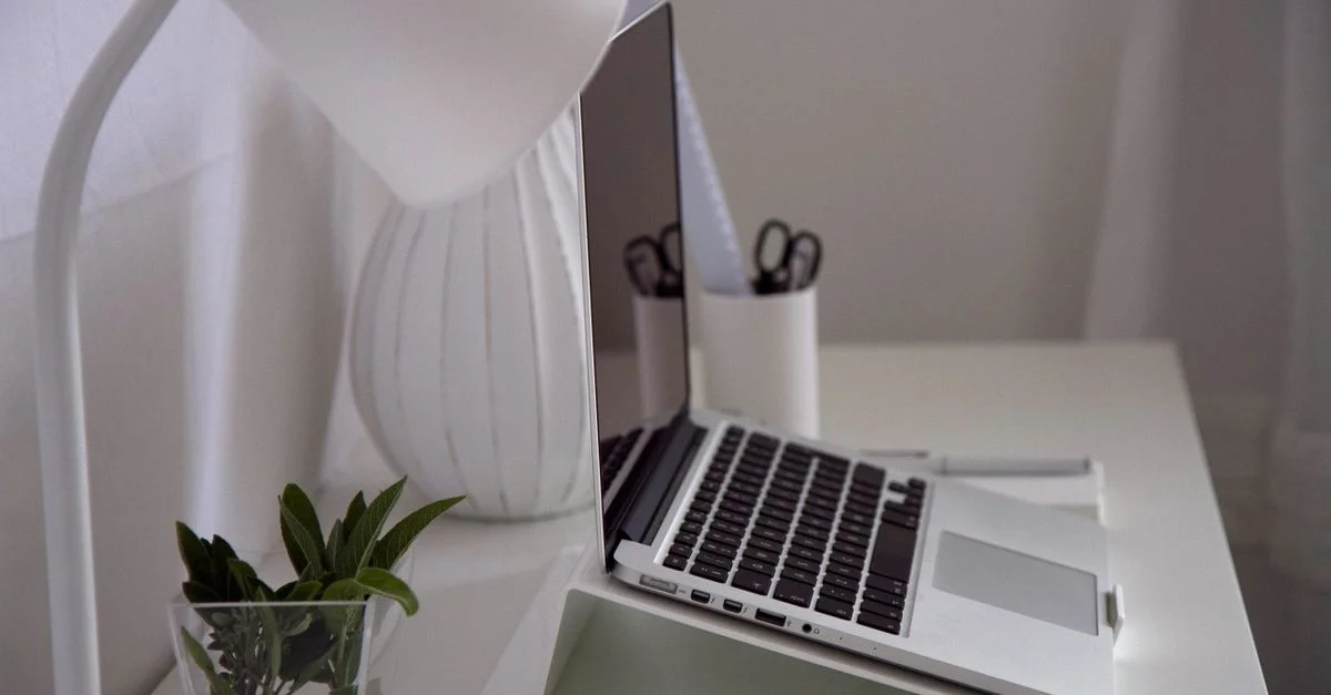 Despacho moderno en casa con ordenador portátil, lámpara de escritorio y planta sobre un escritorio blanco.