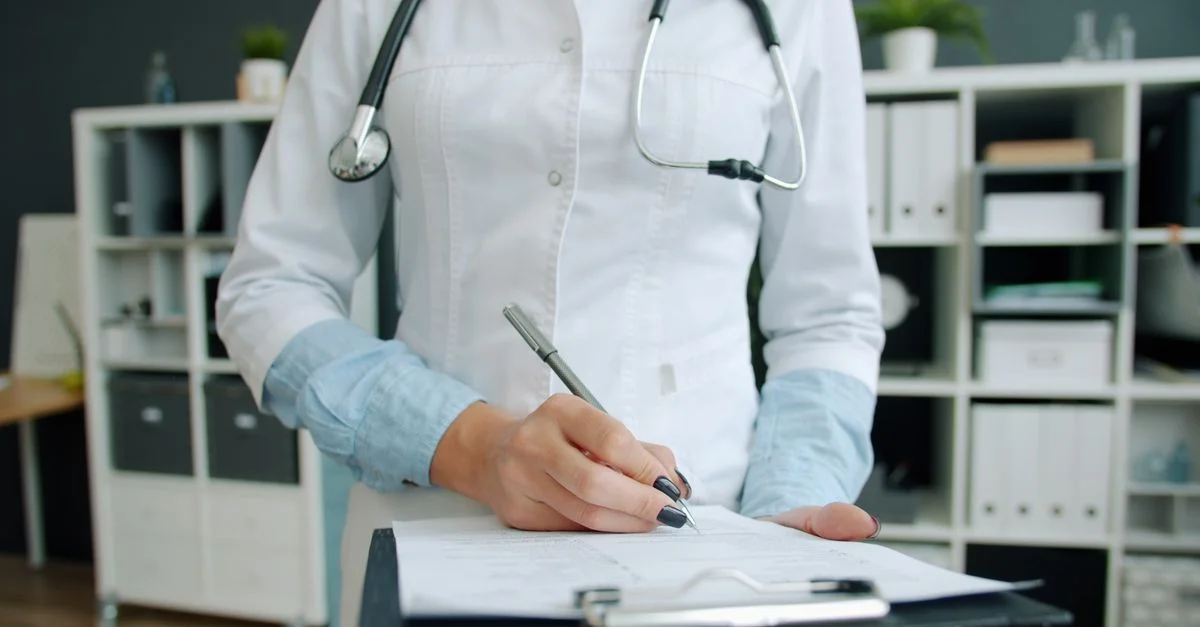 Un médecin en blouse blanche prend des notes sur un bloc-notes dans son bureau.