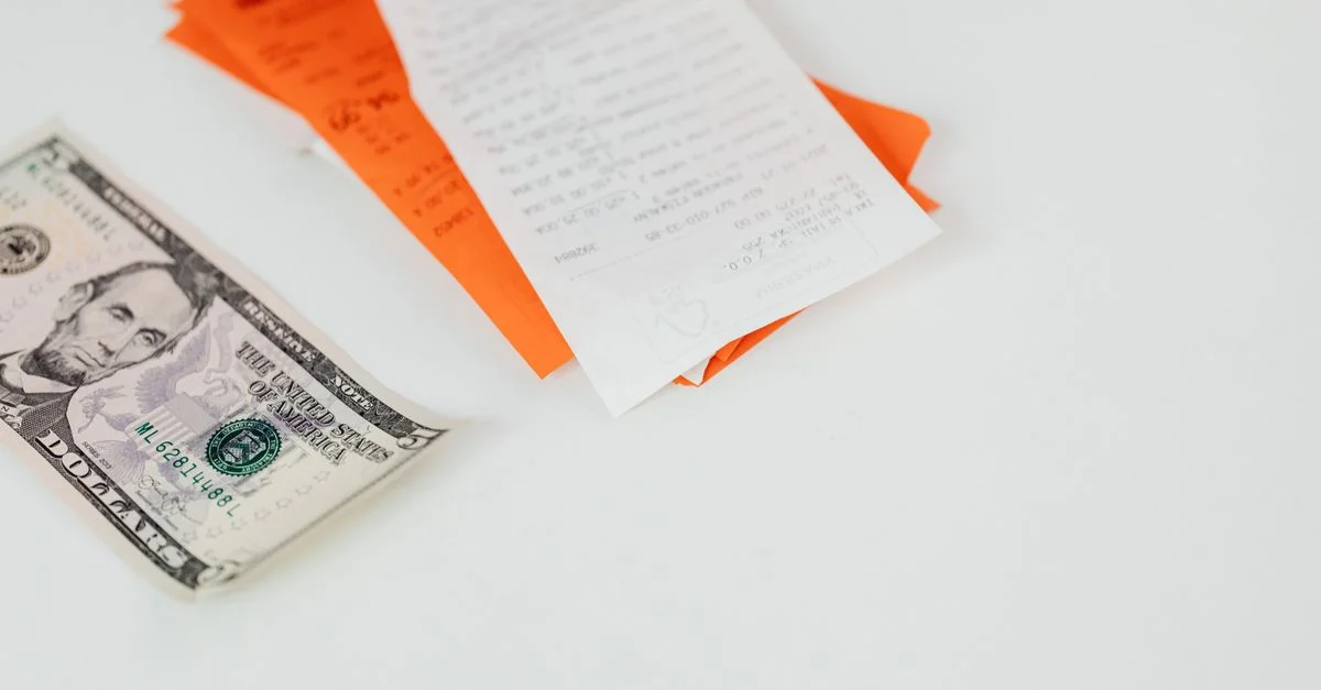 Un billete de cinco dólares y recibos sobre una superficie blanca, enfatizando finanzas y gastos.