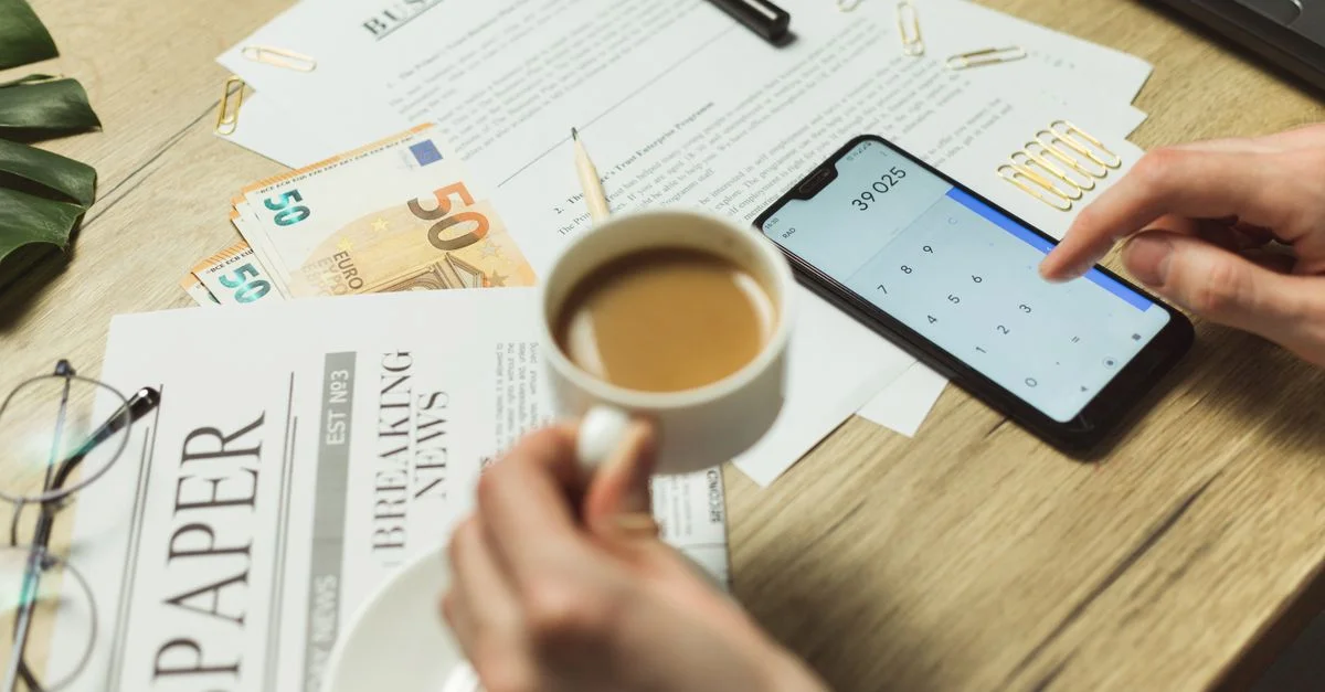 Vista en ángulo alto de un espacio de trabajo empresarial con documentos, café, moneda y calculadora de smartphone.