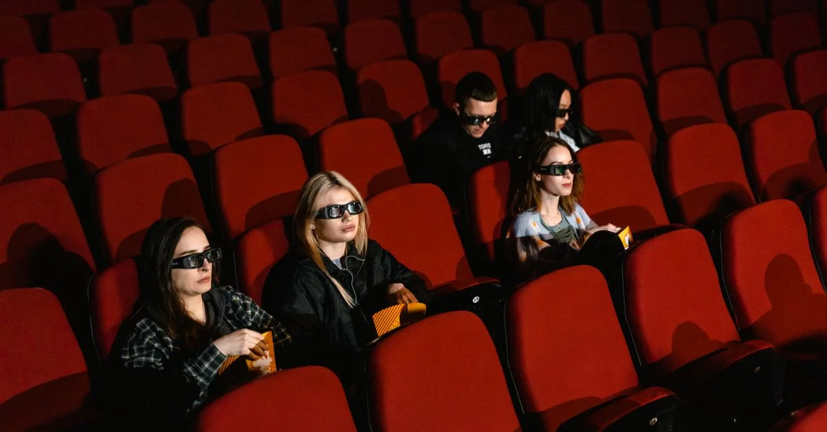Grupo de personas usando gafas 3D en un cine viendo una película y disfrutando de palomitas.