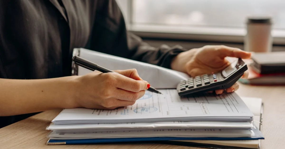 Primer plano de una persona usando una calculadora con documentos financieros en una oficina.