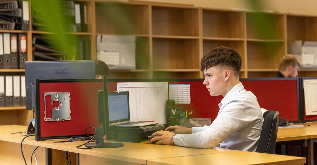 Un joven concentrado tecleando en una computadora en un entorno de oficina contemporáneo.