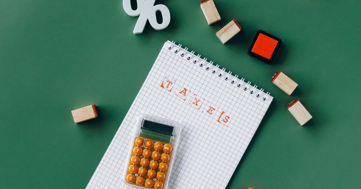 Plano cenital de elementos esenciales para impuestos con calculadora, cuaderno y sellos sobre un fondo verde.