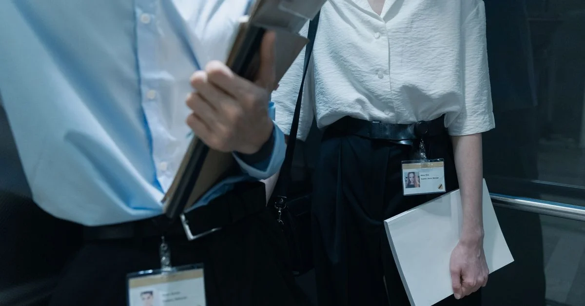 Deux professionnels dans un ascenseur portant des documents, affichant une tenue de bureau.
