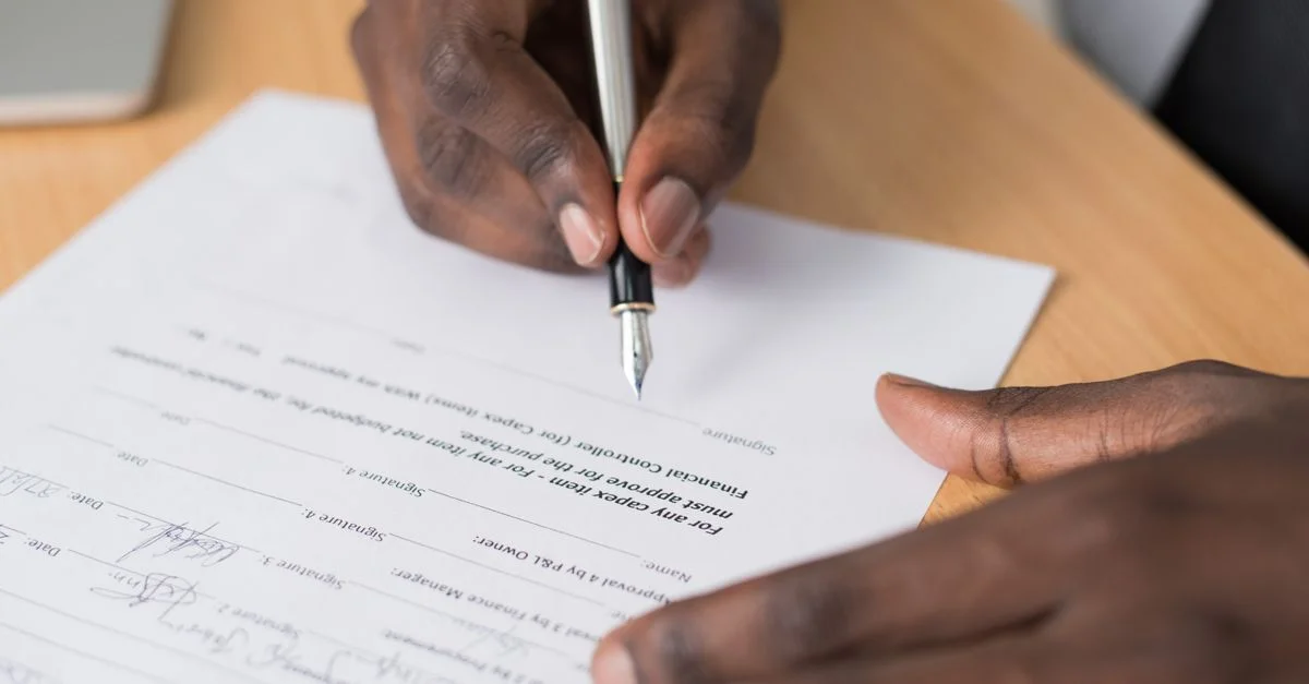 Primer plano de las manos de un hombre firmando un documento formal en interiores.
