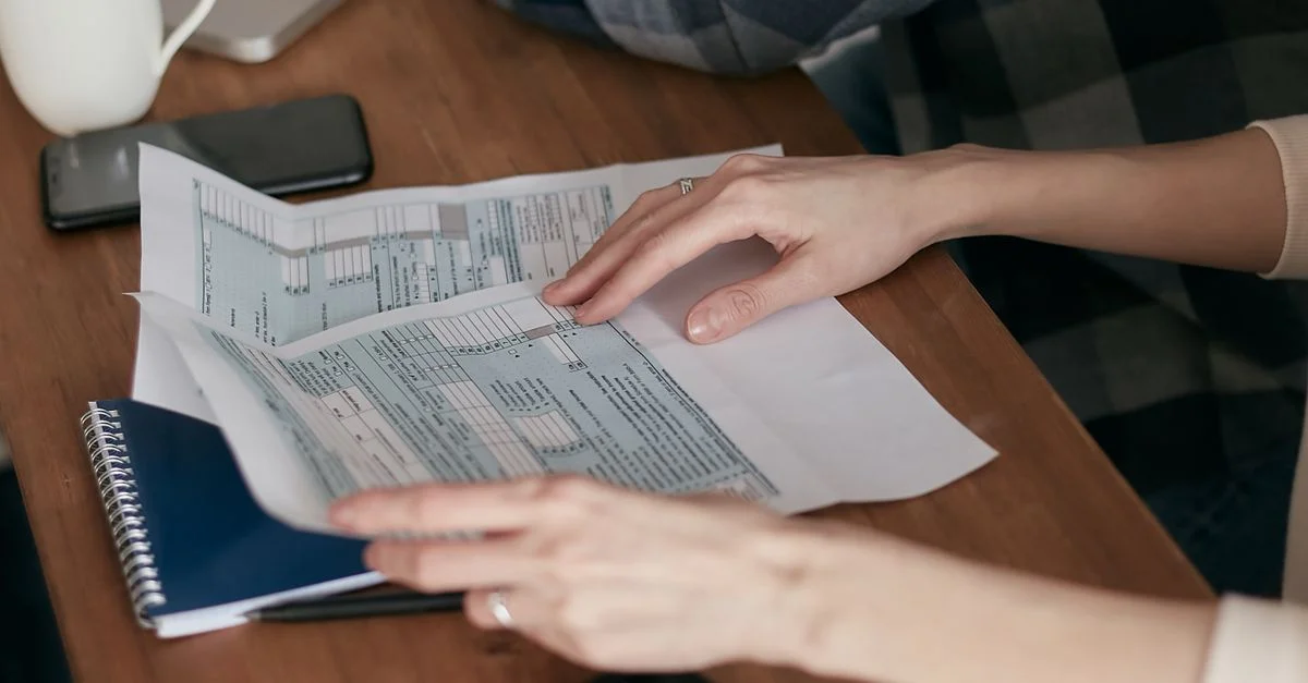 Gros plan sur des mains organisant des formulaires fiscaux sur un bureau avec une calculatrice, un ordinateur portable et un carnet.