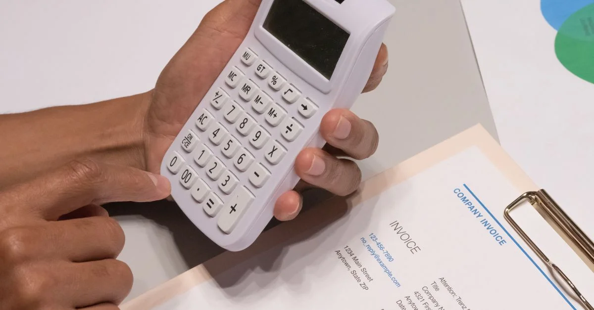 Primer plano de manos usando una calculadora junto a una factura de empresa, representando un concepto de cálculo financiero.