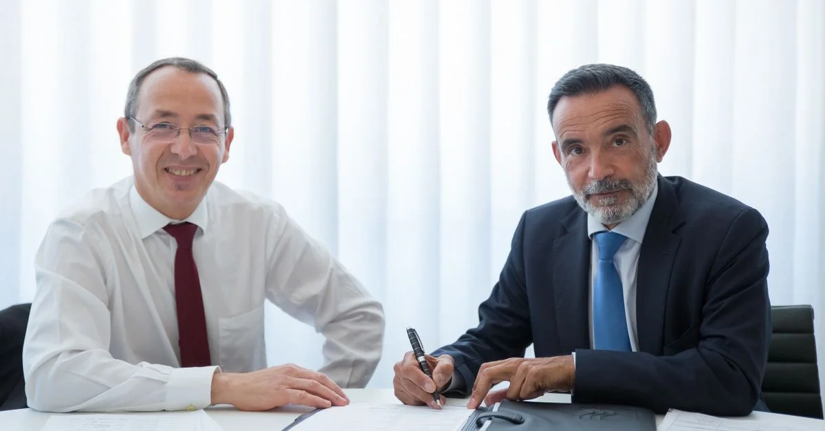 Dos empresarios discutiendo y firmando documentos en una mesa de oficina iluminada.