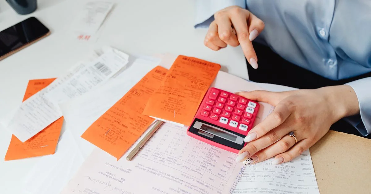 Empresaria calcula gastos utilizando recibos y calculadora en el escritorio. Ideal para temas de finanzas y contabilidad.